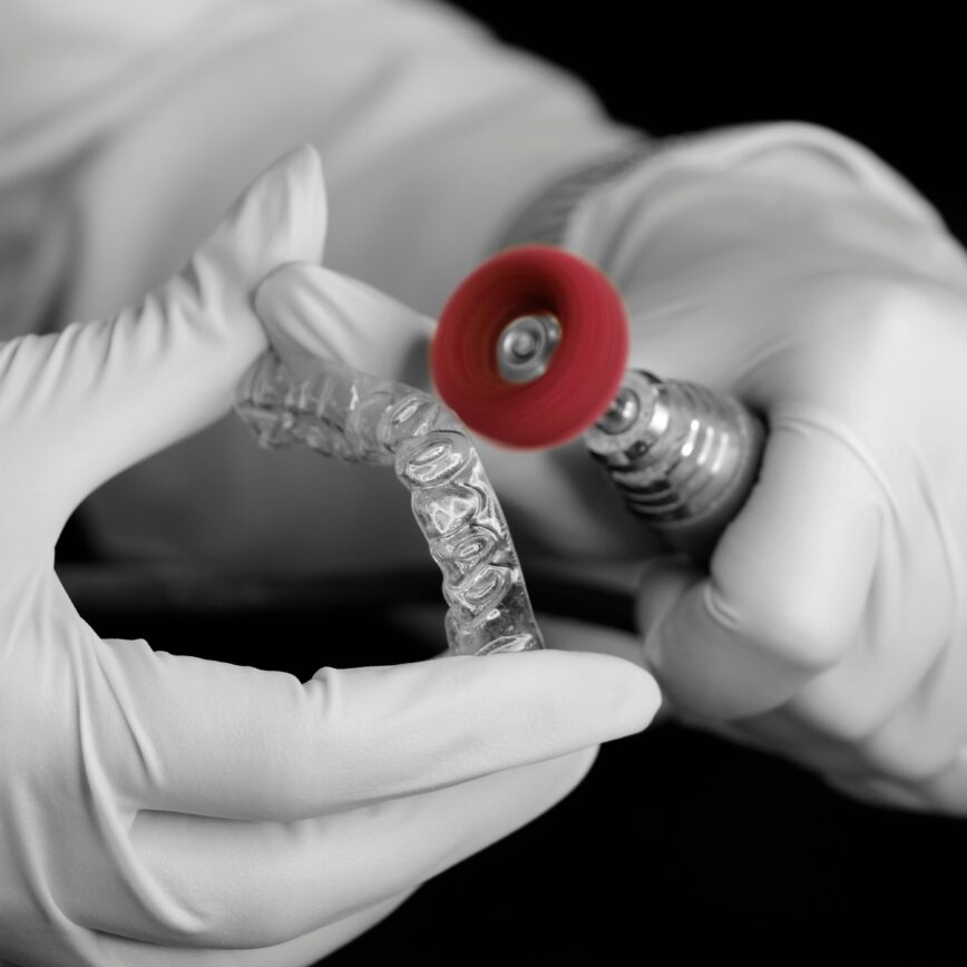 A dental technician uses a grinder to polish a clear aligner in a laboratory setting.