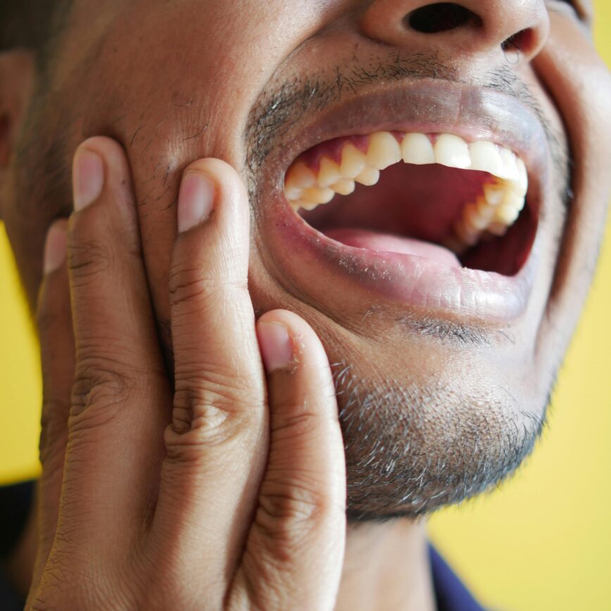 Close-up of a man holding his cheek, displaying a wide open mouth against a yellow background.
