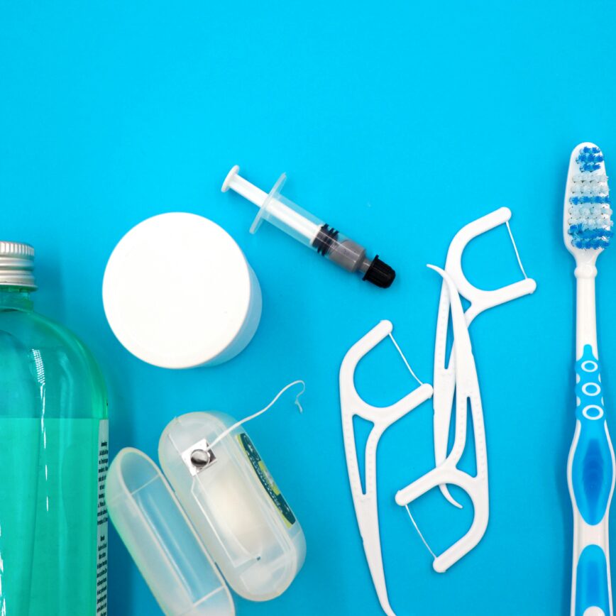 Flat lay of oral hygiene essentials including toothbrushes, floss, and mouthwash on a blue surface.