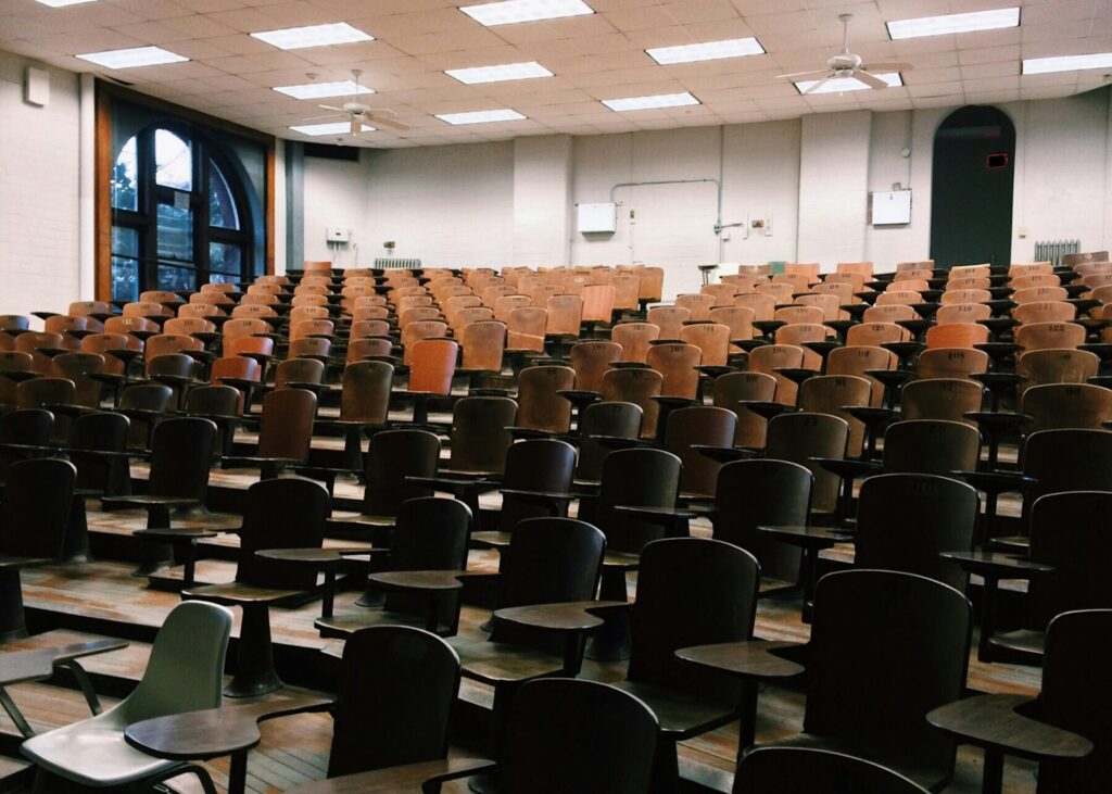 pexels-photo-356065-356065-1 Empty university lecture hall with wooden chairs and large windows.