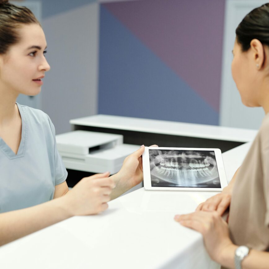 A dentist explains X-ray results to a patient using a tablet in a modern dental clinic.