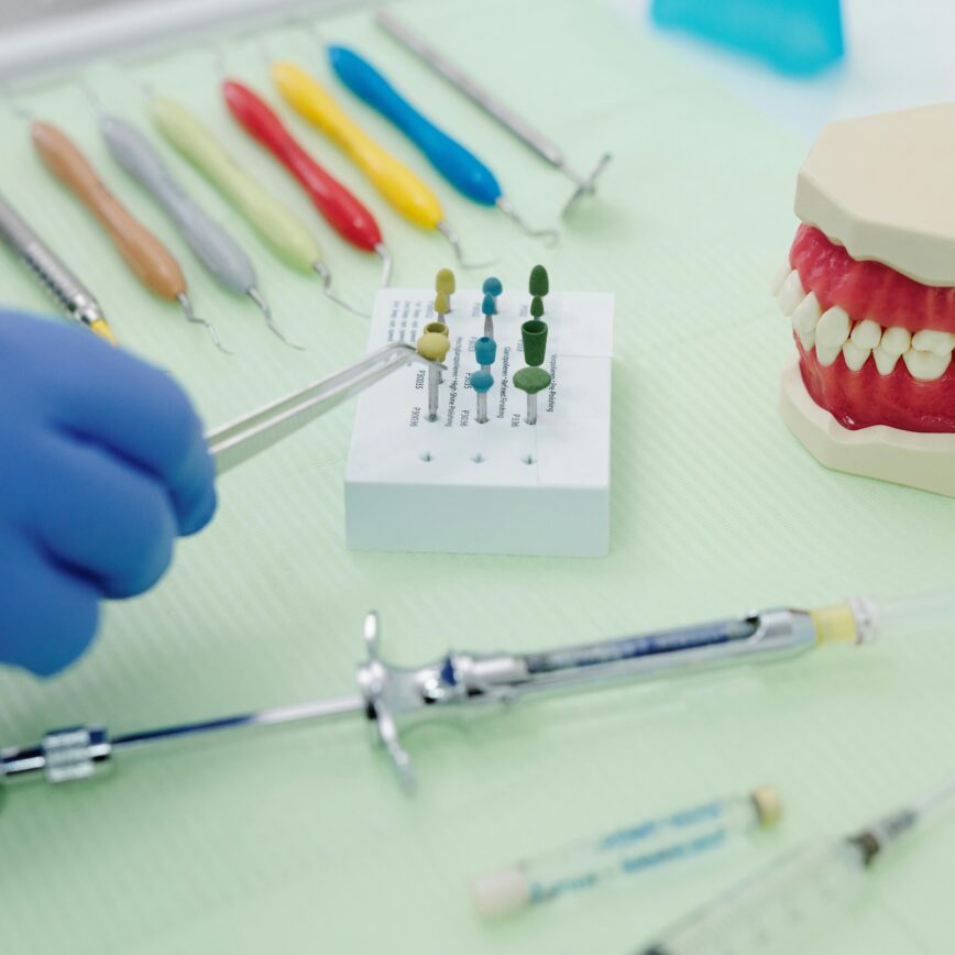 From above of crop faceless orthodontist in latex gloves and tweezers working at medical table with cast jaw and set of syringes near periodontal scalers