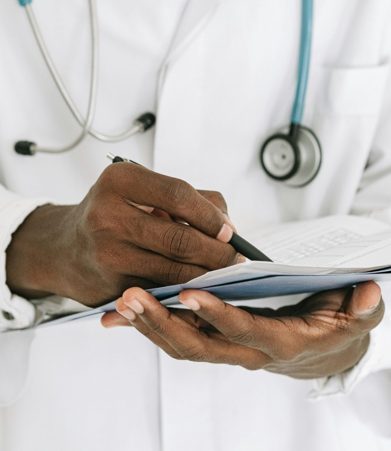 Professional doctor writing on a clipboard with a stethoscope in a medical office.