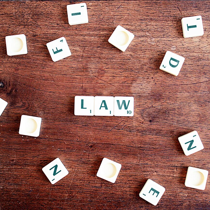 Scrabble tiles spelling 'LAW' on a wooden table, symbolizing connections to education and legality.