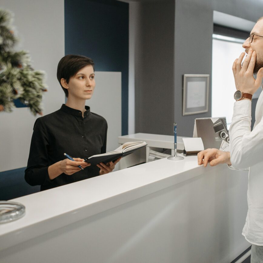A receptionist assists a patient with a toothache at a dental clinic's front desk.