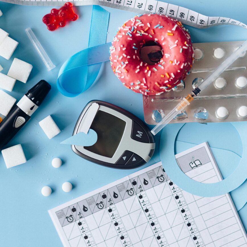 Still life image of diabetes management equipment, sweets, and medication arranged artfully on a blue background.
