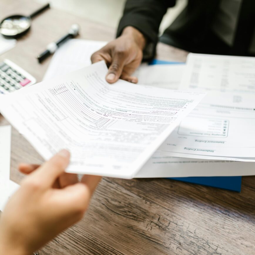Two professionals exchanging documents in an office setting, focusing on paperwork and data analysis.