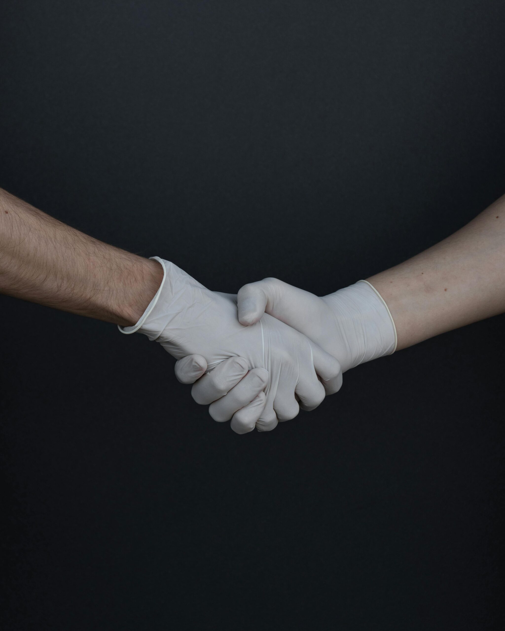 Two people shaking hands while wearing latex gloves, illustrating safety and protection.