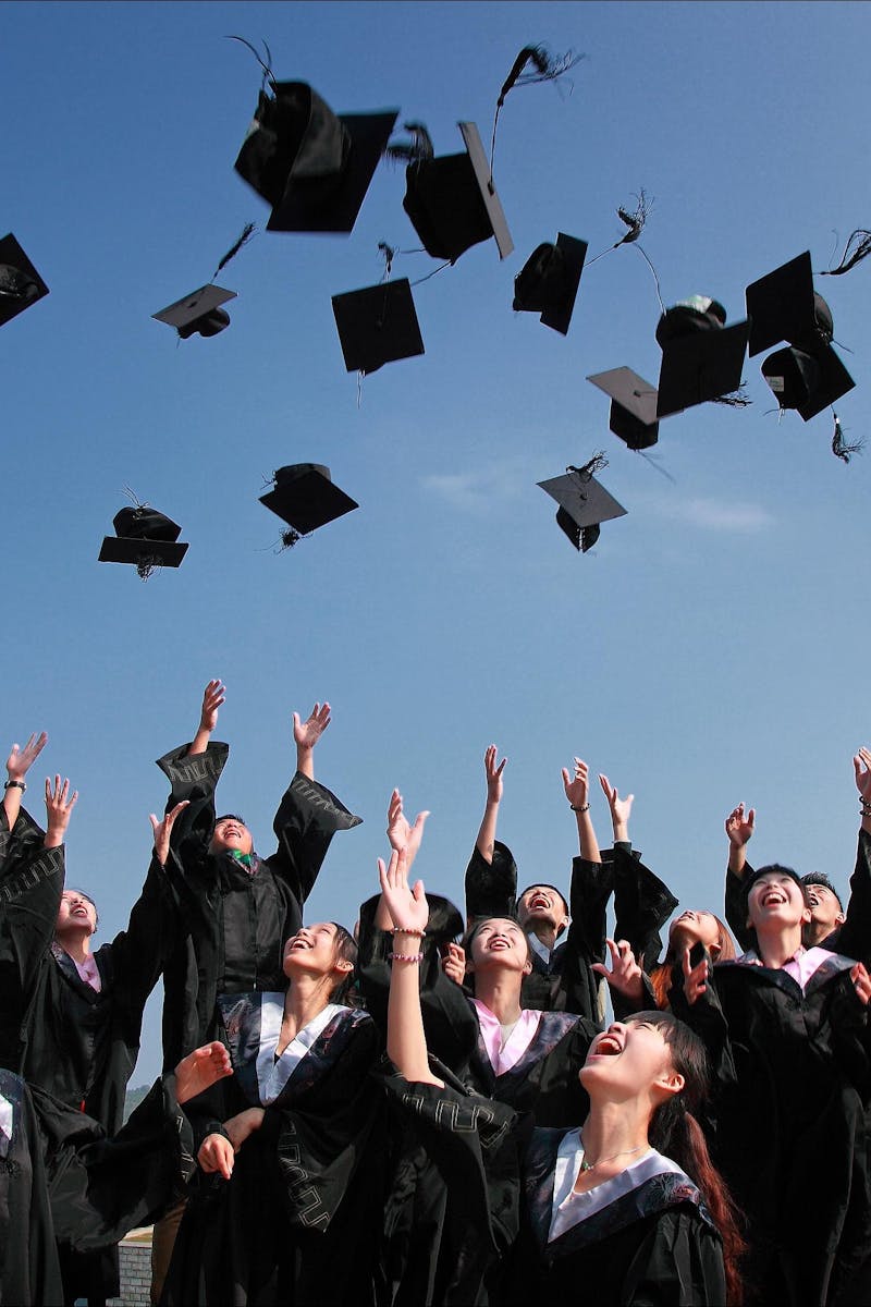 Group of graduates celebrating by throwing caps in the air during a sunny day.